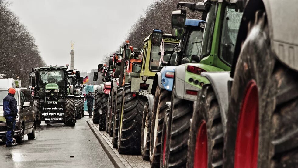 Farmers' protests Photo: Tractors stand in a long row on the street in Berlin, with the Berlin Victory Column in the background and a sign with a protest message in front.
