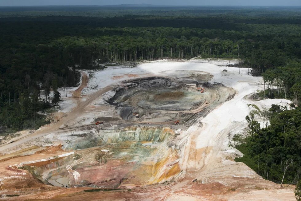 Goldmine in Guyana Große offene Mine mit mehreren Baggern am Rand eines dichten Waldgebiets, Boden zeigt verschiedene Farbnuancen.