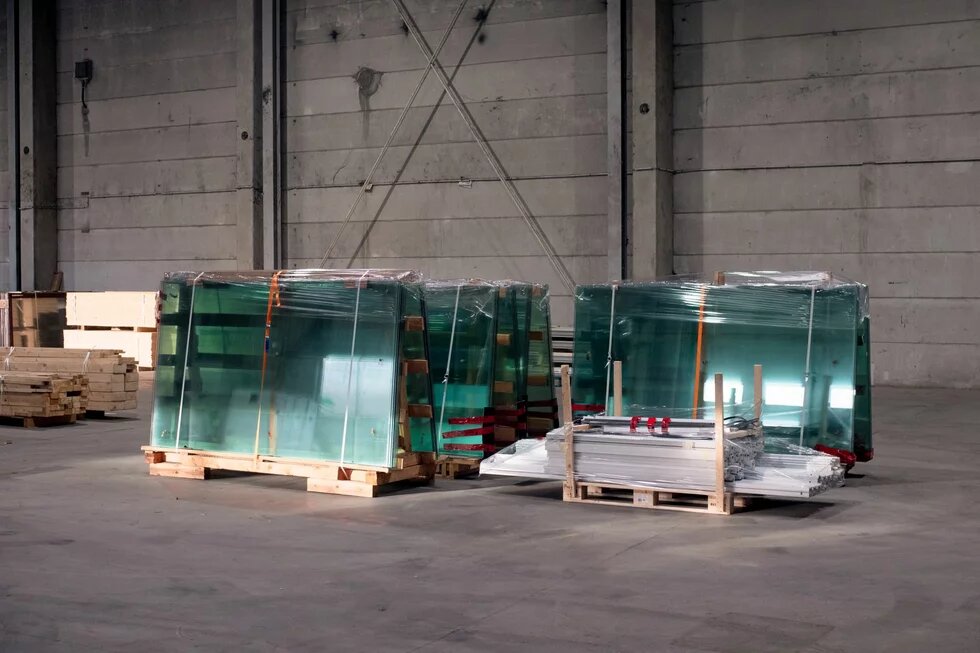 Wiedergewonne Baumaterialien Mehrere große Glasplatten stehen auf Paletten in einer leeren Lagerhalle, teils mit Folie umwickelt.