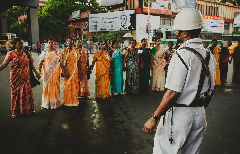 Several women are standing on the street holding hands, facing a uniformed police officer wearing a helmet.