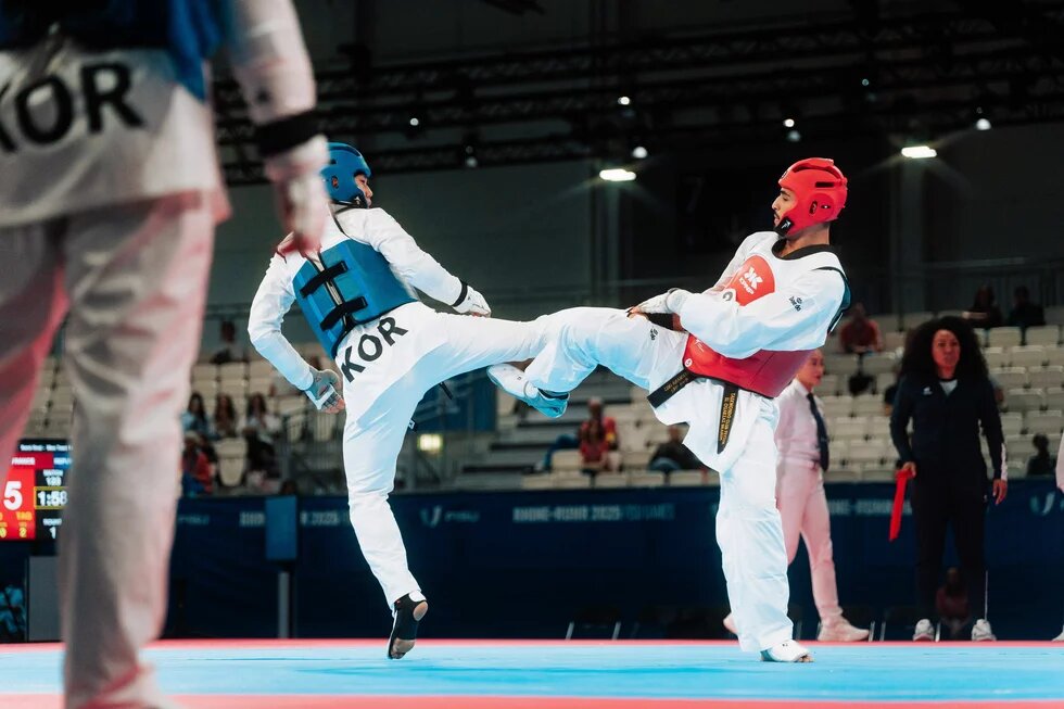 Taekwondo Two taekwondo fighters exchange kicks mid-air during a match; one wears blue gear, the other red. Judges and spectators in the background.