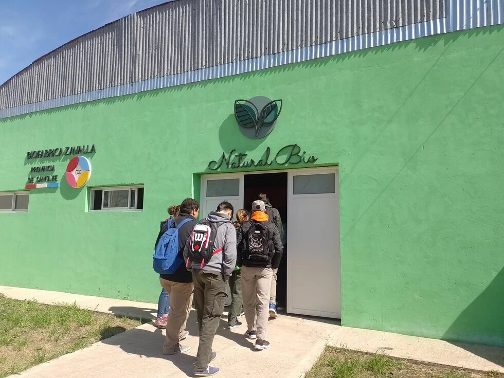 Several people enter a green building labeled "Natural Bio".