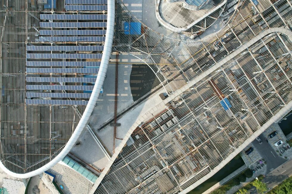 Aerial view of a curved building under construction with solar panels and a grid-like roof structure.