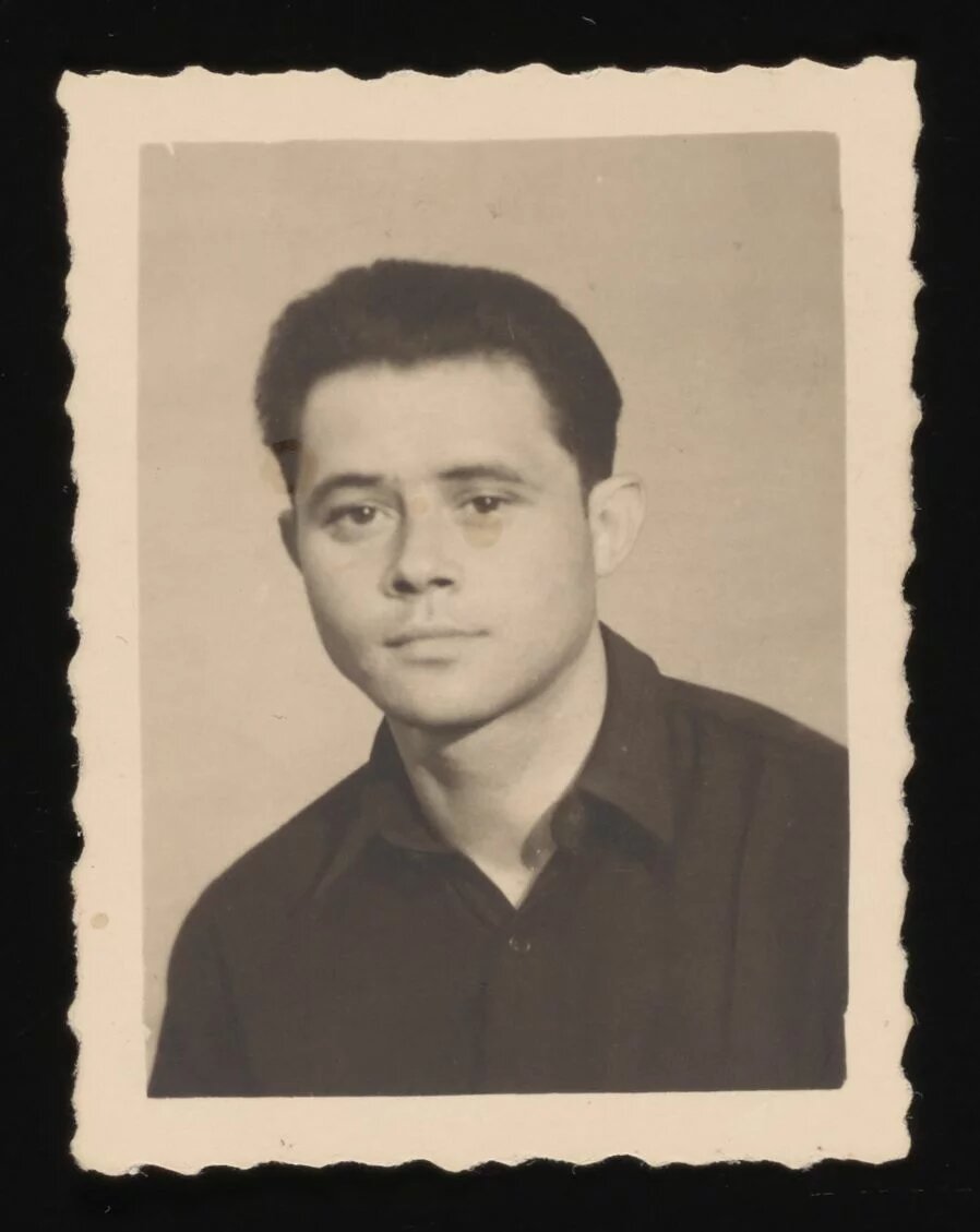 Porträtfoto eines jungen Mannes mit kurzen, dunklen Haaren, ovalem Gesicht, dunklen Augen, mit dunklem Hemd vor neutralem Hintergrund