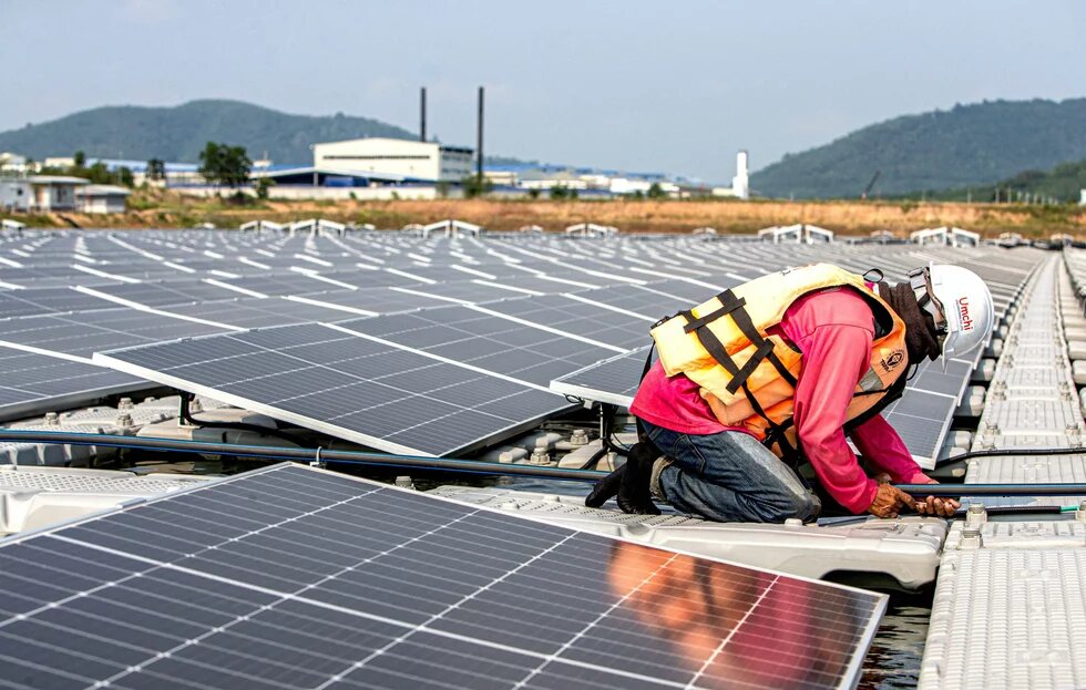 Eine Person kniet zwischen Solarpaneelen und arbeitet mit Werkzeug auf einer schwimmenden Plattform.