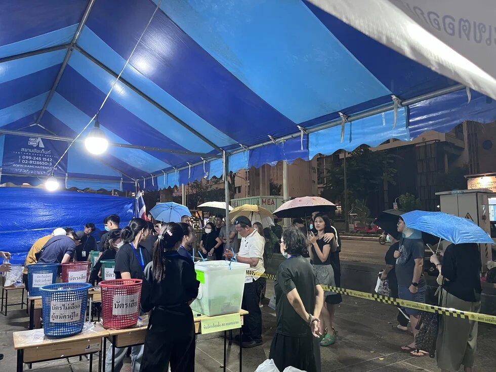 Ein blaues Zelt mit Wahlurnen, Menschen geben ihre Stimme ab.