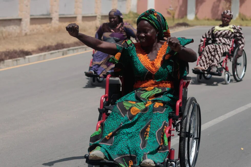 Das Foto zeigt mehrere Frauen, die in Rollstühlen auf einer Straße fahren.