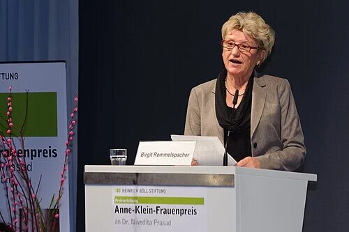 Birgit Rommelspacher spricht an Rednerpult; Namensschild Birgit Rommelspacher; vorne Text Anne-Klein-Frauenpreis; Mikrofon, Glas Wasser; Bühne innen.