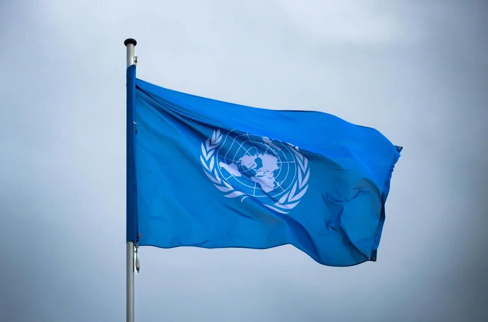 Flagge der UN am Fahnenmast weht im Wind, im Hintergrund der Himmel.