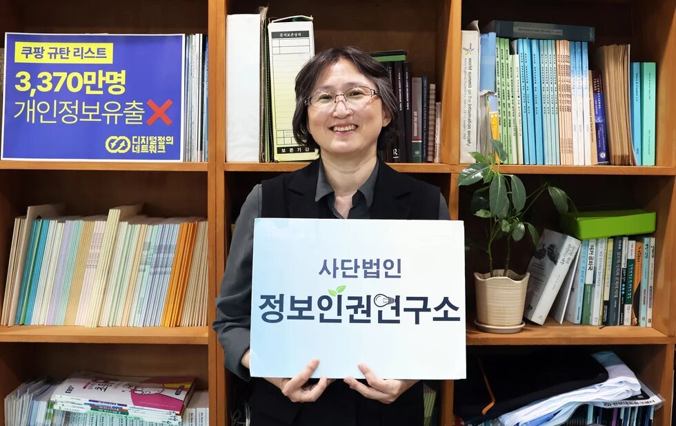 Yeo-Kyeong Chang, Executive Director of the Institute for Digital Rights holding a poster with korean lettering in front of a bookshelf.