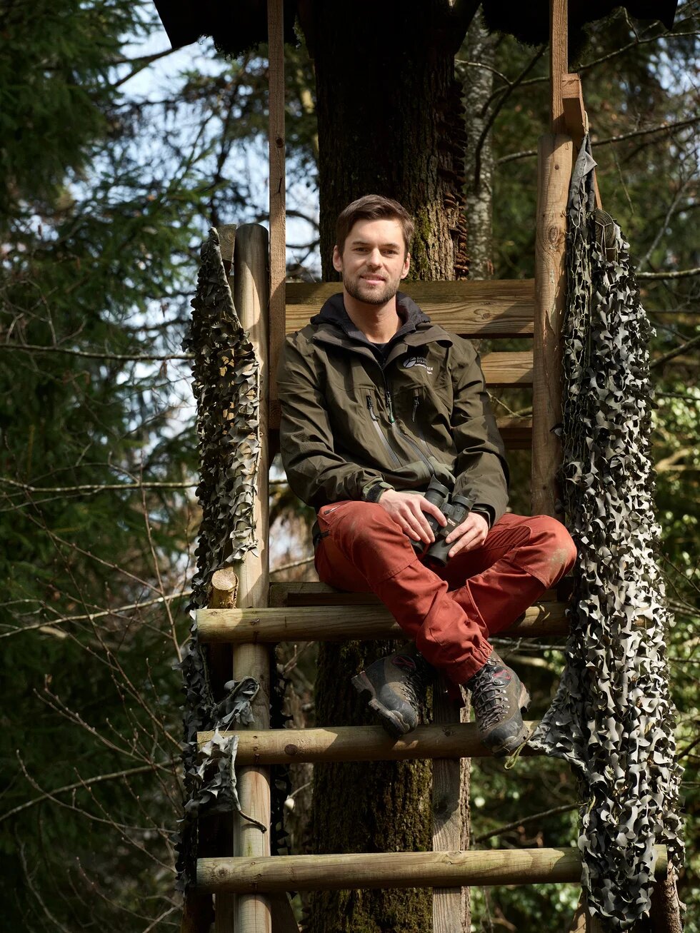 Lukas sitzt auf einem Jägerstand im Wald.
