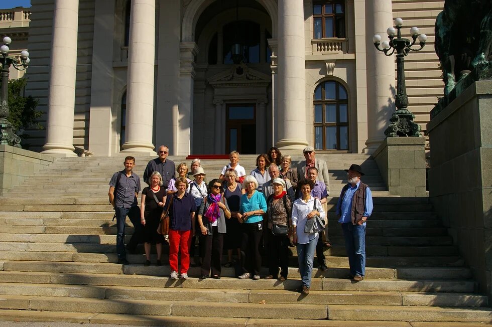 Etwa 20 Personen stehen auf einer breiten Freitreppe vor einem repräsentativen Gebäude mit hohen Säulen und posieren für ein Gruppenfoto.