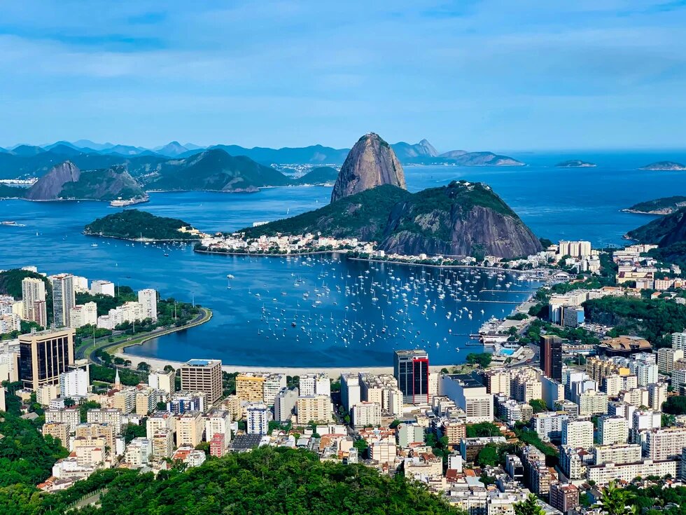 Blick über Rio de Janeiro mit Zuckerhut, Bucht voller Boote, Hochhäusern und bewaldeten Hügeln bis zum Meer.