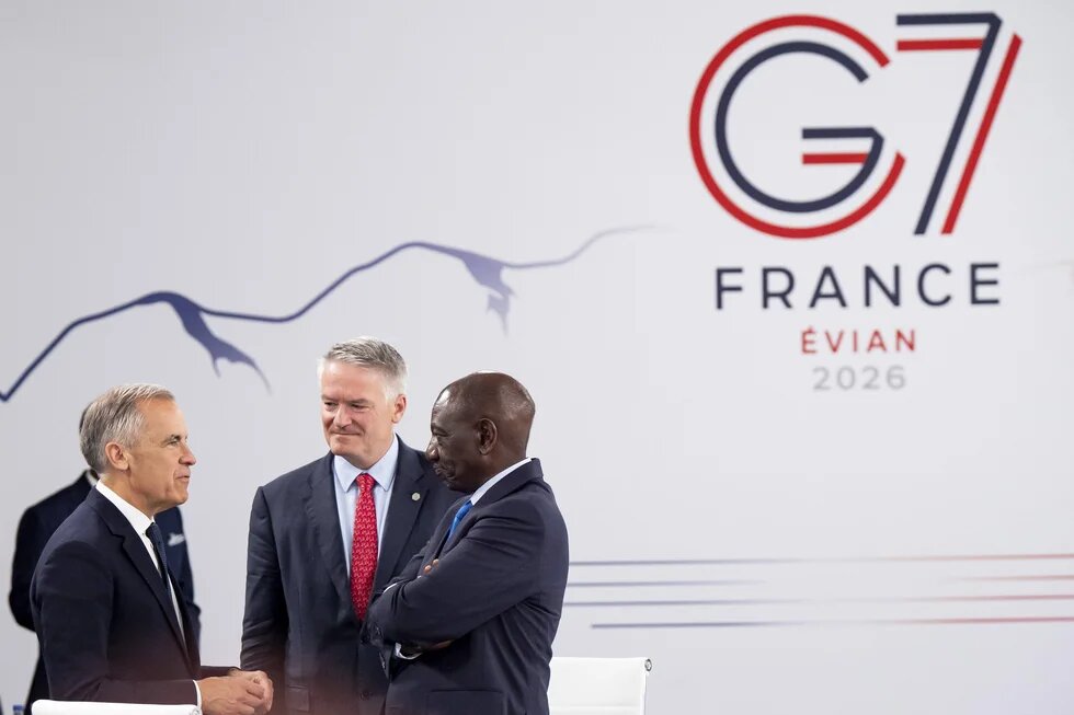 Drei Männer im Anzug sprechen vor einer Wand mit G7-Logo und der Aufschrift „FRANCE EVIAN 2026“.