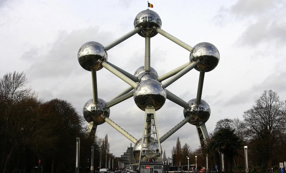 Atomium in Brüssel mit verbundenen Metallkugeln, von Bäumen gesäumter Allee und bewölktem Himmel.