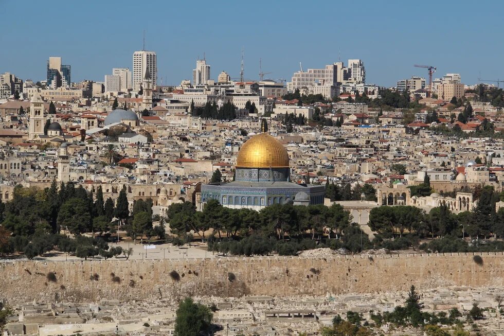 Blick über Jerusalems Altstadt mit dem Felsendom im Zentrum, Stadtmauer, Bäumen sowie dicht bebauten Wohn- und Hochhausvierteln.
