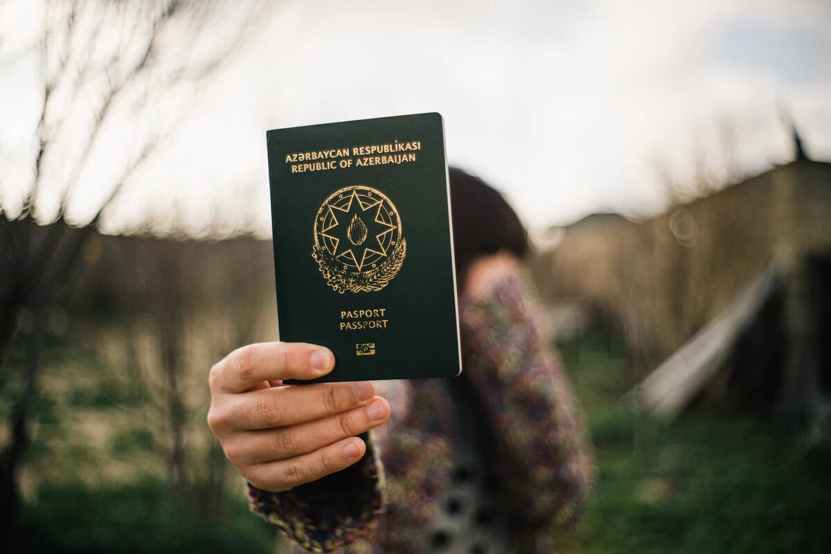 Person hält einen aserbaidschanischen Reisepass in die Kamera, Hintergrund unscharf.