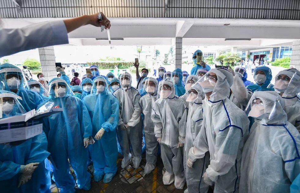 Gruppe von Personen in blauer und weißer Schutzkleidung schaut auf ein hochgehaltenes Röhrchen.