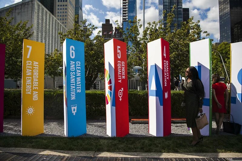 Große bunte Säulen mit UN-Nachhaltigkeitszielen im Freien, u.a. „Clean Water“, „Gender Equality“. Eine Person steht daneben.