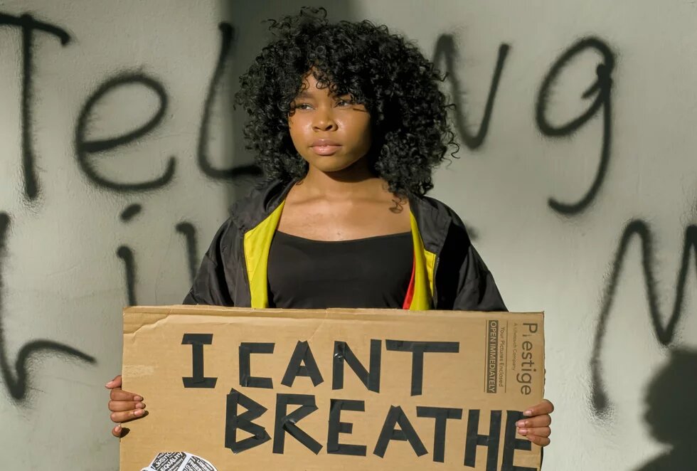 Eine jnge Frau hält ein Plakat. Da steht "I can't breathe" drauf