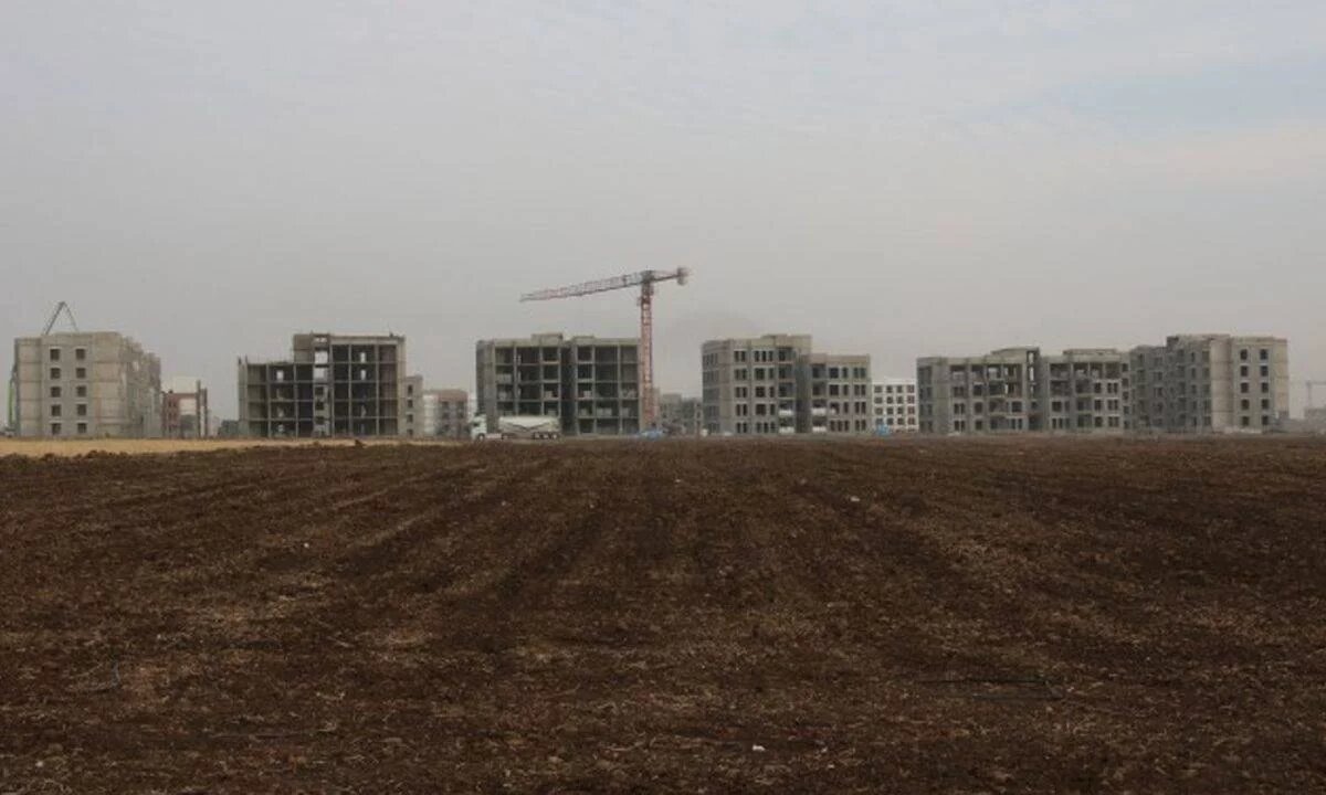 Eine Baustelle mit mehreren im Bau befindlichen Wohngebäuden. Im Vordergrund ein braches Feld, im Hintergrund ein Baukran.