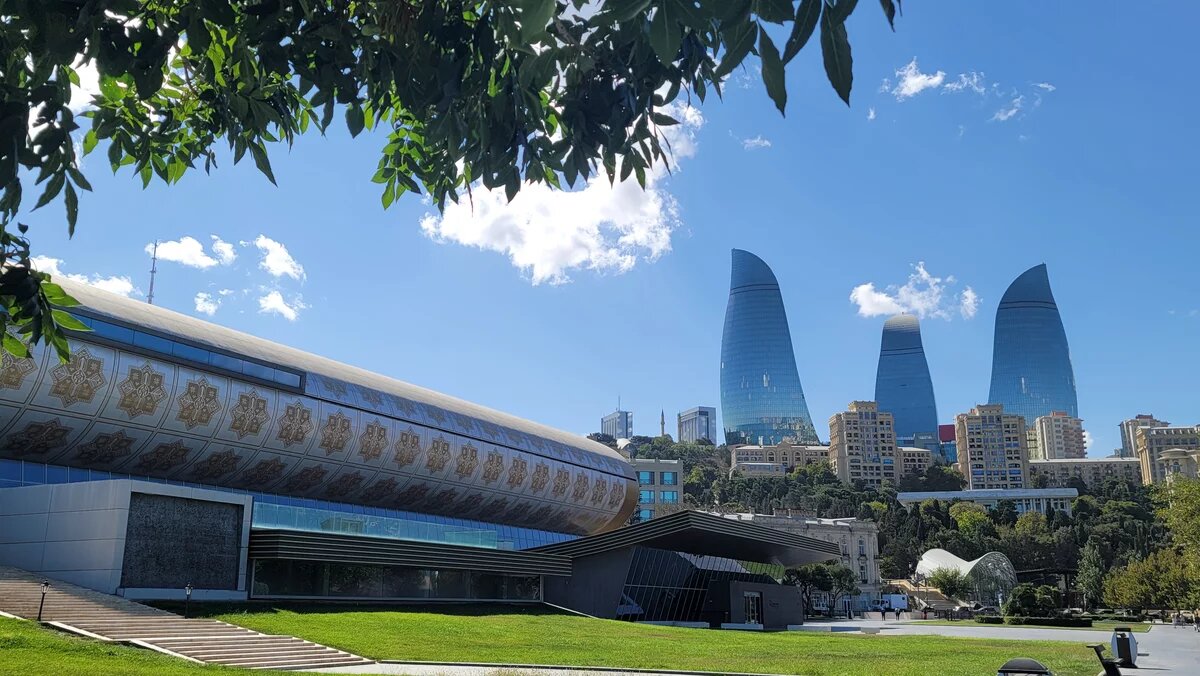 Modernes Gebäude mit Mustern im Vordergrund, dahinter die drei markanten Hochhäuser der Flame Towers in Baku.