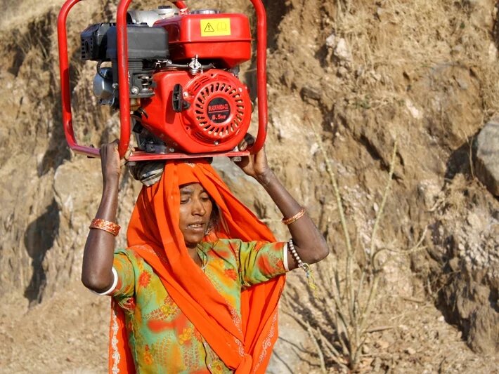 The women of the mountain villages in Rajasthan, India, carry 70 lbs. (or 32kgs) of wood on their heads for cooking every day. This woman is carrying a generator for repair in a nearby village The women of the mountain villages in Rajasthan, India, carry 70 lbs. (or 32kgs) of wood on their heads for cooking every day. This woman is carrying a generator for repair in a nearby village