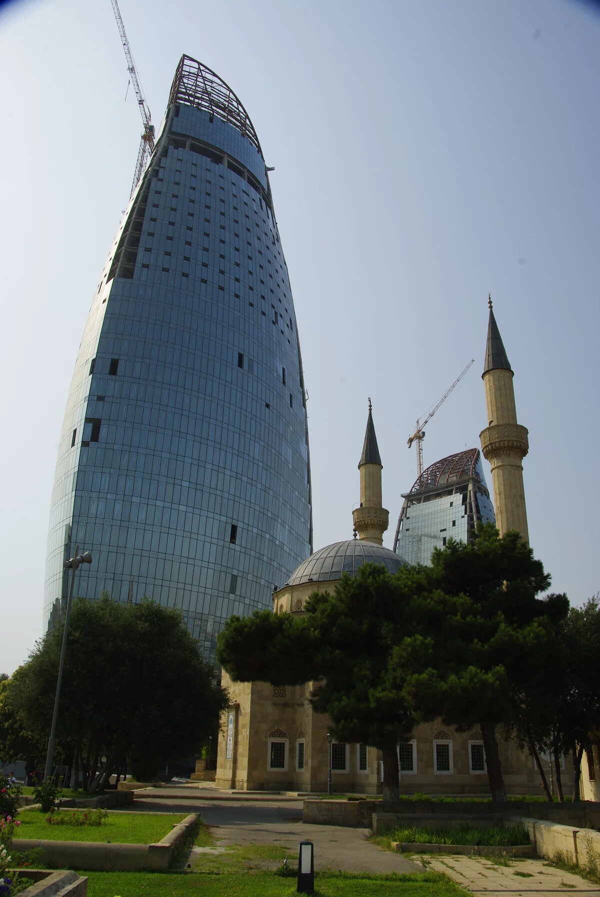 a newly built skyscraper overshadows an old mosque near martyr's alley in baku a newly built skyscraper overshadows an old mosque near martyr's alley in baku