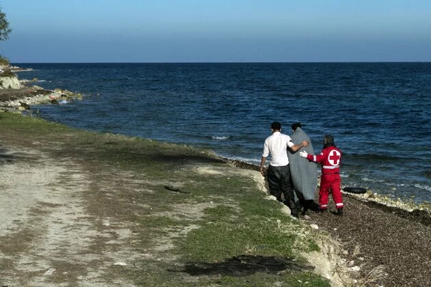 Member of Greek Red Cross helps an Afghan refugee who has just arrived from Turkey with an inflatable boat in the area of airport of Mytilene, Lesvos Island, Greece Member of Greek Red Cross helps an Afghan refugee who has just arrived from Turkey with an inflatable boat in the area of airport of Mytilene, Lesvos Island, Greece