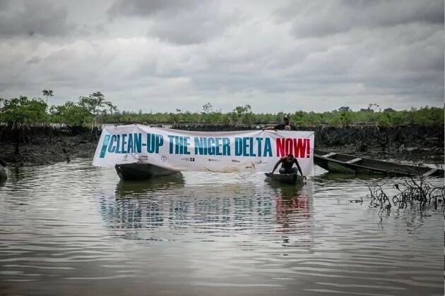 Aktivisten/innen auf dem Fluss mit Transparent "Clean-up the Niger Delta now"