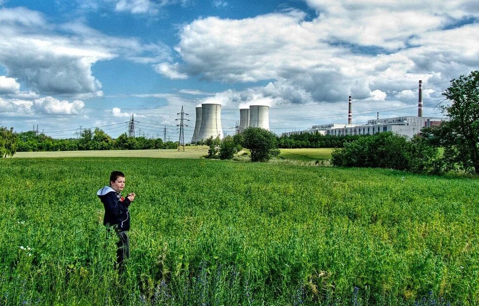 Wie steht der Mensch zur Natur? Ein Junge, stehend in grünem Feld, vor einem AKW