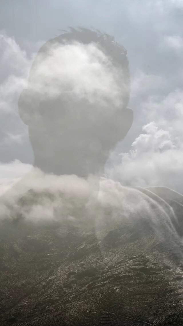 Doppelbelichtung eines Kopfes im Profil und einer Berglandschaft, überlagert von Wolken.