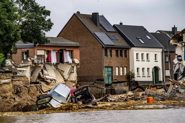Zerstörte Häuser und Autos liegen zwischen Schlamm und Trümmern am Rand einer überfluteten Straße.
