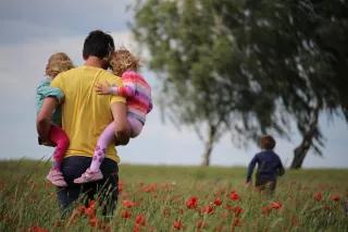 Familienpolitik in Ost- und Westdeutschland: Ein Mann trägt zwei Kinder durch ein Feld