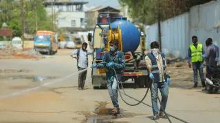 Männer mit Masken reinigen die leeren Straßen in einer Stadt in Indien mit Wasser