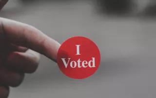 I Voted One hand is holding a sticker with "I Voted" written on it against a blurred background.