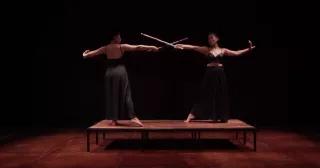 Two women fencing with sticks on a small stage