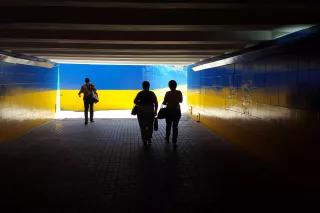 Drei Personen in einer dunklen Unterführung, die Wände sind in Blau und Gelb gestrichen