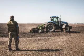 Ein ukrainischer Soldat betrachtet einen Traktor, der ein Feld während des Kriegs in der Ukraine pflügt