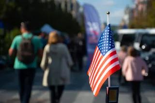 New York, USA, amerikanische Flagge weht im Vordergrund - Menschen und Autos im Hintergrund