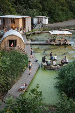 Viele Menschen sitzen auf Bänke im Wasser beim Floating University. Es gibt auch eine Hütte und einen Laufweg über das Wasser