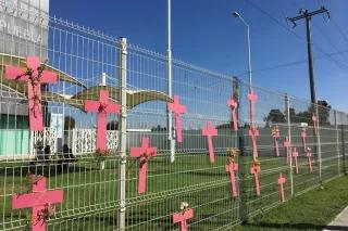 Mehrere rosane Kreuze und Blumen hängen an einem Zaun Gedenkstaette Verschwindenlassen