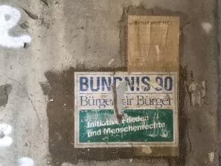 Auf einer grauen Betonwand klebt ein altes, zerschlissenes Wahlplakat, darauf steht: "Bündnis 90 Bürger für Bürger Initiative Frieden und Menschenrechte