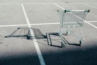 Ein leere Einkaufswagen steht auf einem leeren Parklatz und wirft einen langen Schatten