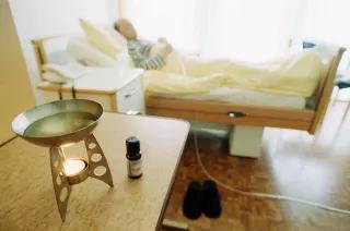 begleitete Sterbehilfe Hospizzimmer, im Vordergrund Aromalampe auf einem Tisch und im Hintergrund etwas verschwommen der Patient im Bett