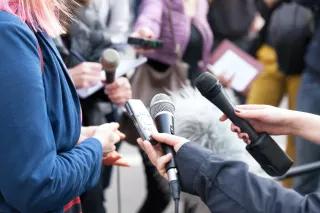 Interview auf einer Pressekonferenz Mehrere Hände strecken einer Person Mikrofone und Aufnahmegeräte entgegen
