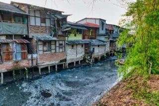 Ein Slum aus vielen aneinander und aufeinander gebauten Hütten, die auf Pfählen an einem verschmutzen Kanal stehen