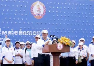 Hun Manet steht auf einer Bühne hinter einem Pult, er trägt ein weißes Hemd und eine weiße Mütze mit dem Logo seiner Partei, dahinter stehen mehrere Menschen mit der gleichen Kleidung