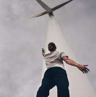 Eine Person steht unterhalb eines Windrads und reckt einen Arm in die Höhe