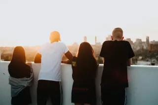 Vier Menschen schauen über eine Mauer in den Sonnenuntergang auf eine Stadt